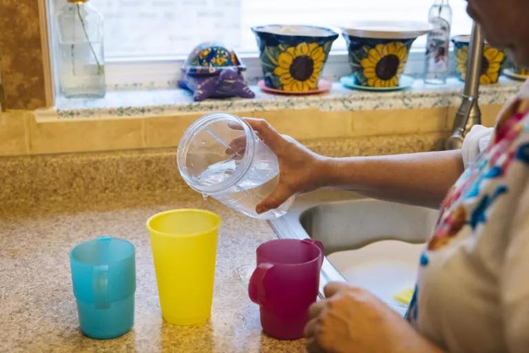 A woman pours water from a large container into small plastic cups