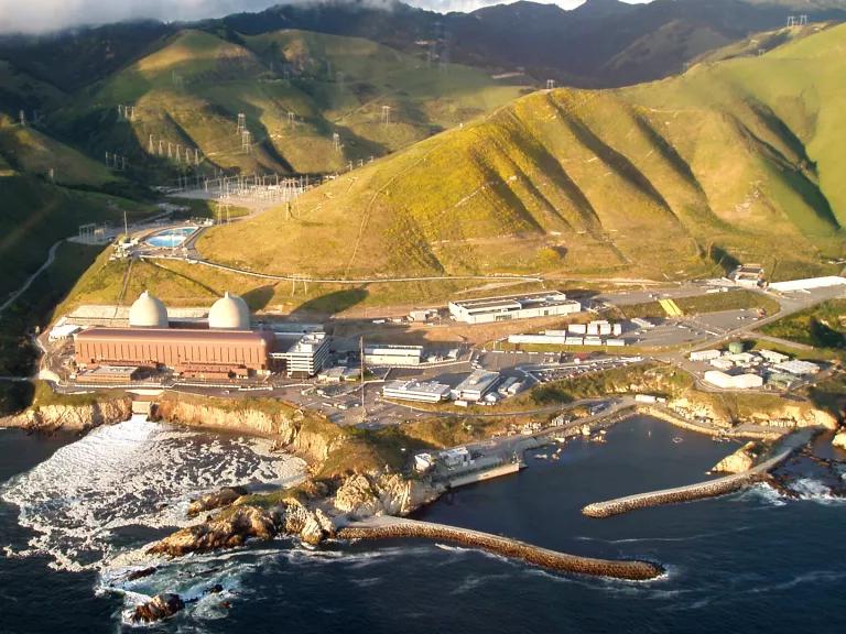 An aerial view of a power plant situated on a coastline with mountains behind it