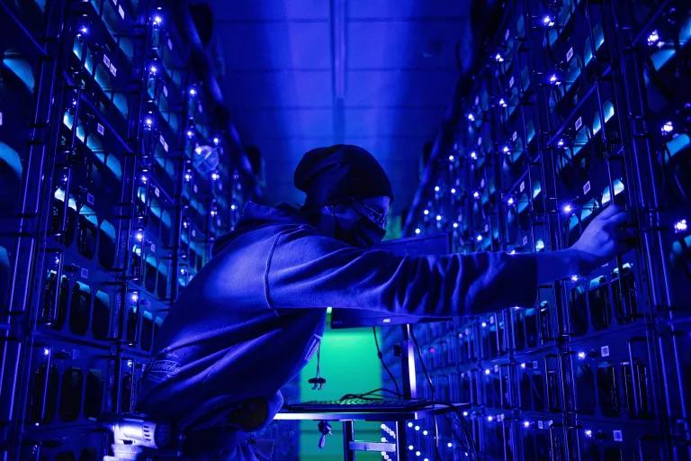 A worker in between stacks of servers in a large, dimly lit room