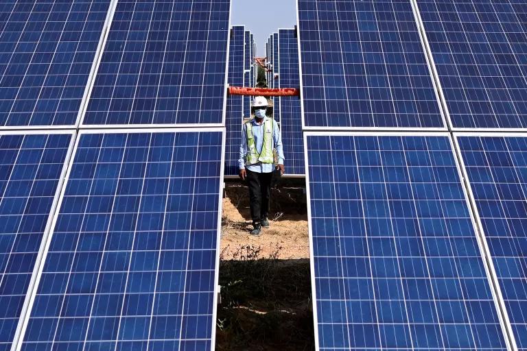 A person walks between the panels of a large solar array