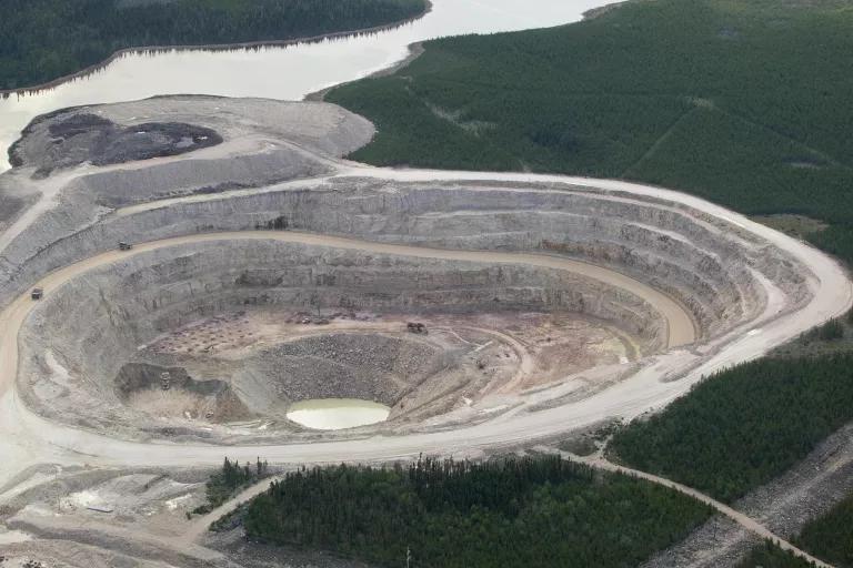 An aerial view of a vast open mine pit, with green land and a body of water surrounding it