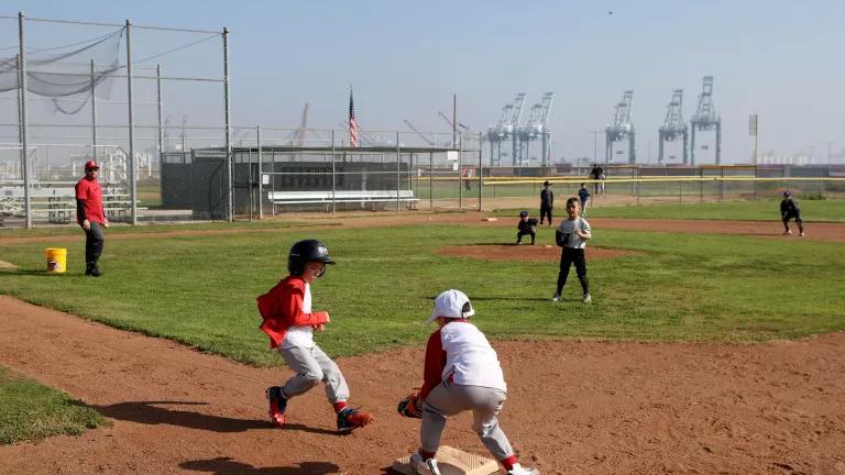 Children play baseball on a field with oil pumpjacks visible in the distance