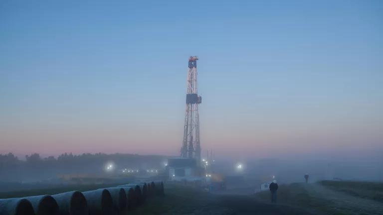 A fracking tower is lit up in the distance under a hazy sky