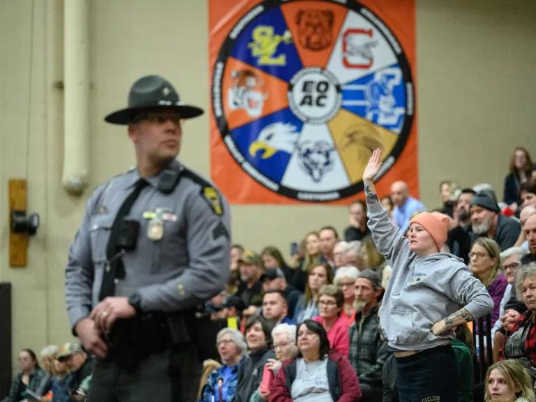 A state trooper stands among a crowd of people seated in an auditorium