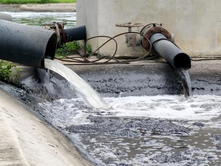Wastewater spilling from pipes into a holding pond.