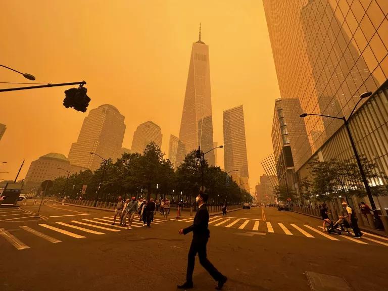 Pedestrians pass New York’s One World Trade Center amid a smokey haze