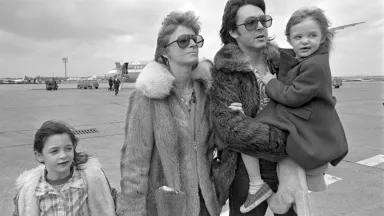 A black and white image of Linda and Paul McCartney on an airfield with two young children