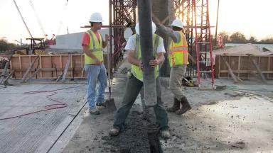 Three workers pour concrete at a construction site