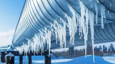 A close-up view of an icicles hanging from a gas pipeline running through a snowy landscape