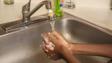 A pair of hands clasped together under a running faucet with soap on the hands