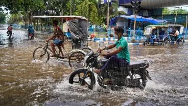 Drivers on tuk-tuks and motorbikes ride through rain and floodwaters
