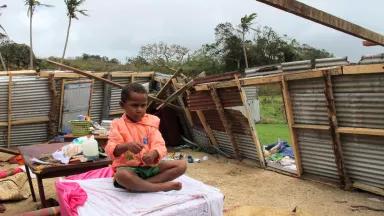 A child sits on a table inside the remains of a home with no roof