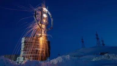 A large metal sculpture being welded on a snowy clearing