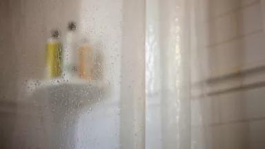 A clear plastic shower curtain hangs in a bathroom shower